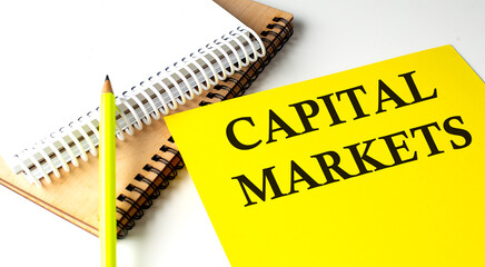 Poster - CAPITAL MARKETS text written on a yellow paper with notebook