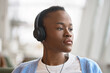 African Black ethnic teenage girl generation z student with short hair sitting indoors, wearing headphones looking away at window, listening new cool music mix, audio book podcast. Close up portrait