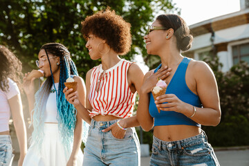 Wall Mural - Group of cheery women eating ice cream while spending time together outdoors