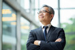 © wolfhound911 - Happy proud prosperous mid aged mature professional Asian business man ceo executive wearing suit standing in office arms crossed looking away thinking of success, leadership, side profile view.