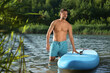 © New Africa - Man standing near SUP board in river water on sunny day