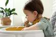 © New Africa - Cute little baby eating healthy food in high chair indoors