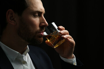 Canvas Print - Man in suit drinking whiskey on black background