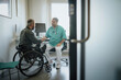 © Maskot - Doctor discussing with male patient sitting in wheelchair at hospital