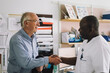 © Maskot - Smiling senior patient shaking hand with mature male doctor after visit in clinic
