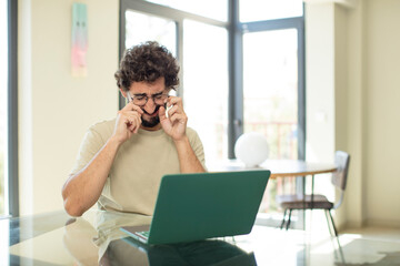 Sticker - young adult bearded man with a laptop looking desperate and frustrated, stressed, unhappy and annoyed, shouting and screaming