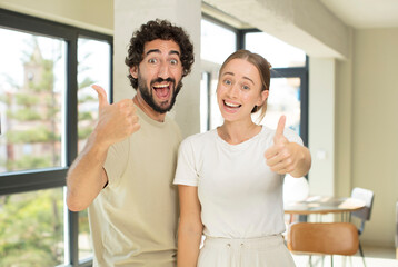 Canvas Print - young adult couple smiling joyfully and looking happy, feeling carefree and positive with both thumbs up