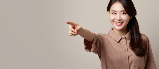 Wall Mural - Asian woman in brown shirt with a smile pointing to blank space for advertising