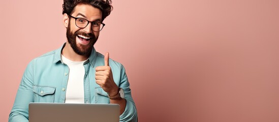 Canvas Print - A happy bearded young man with laptop smiling and pointing to the side and upwards displaying an object in empty area