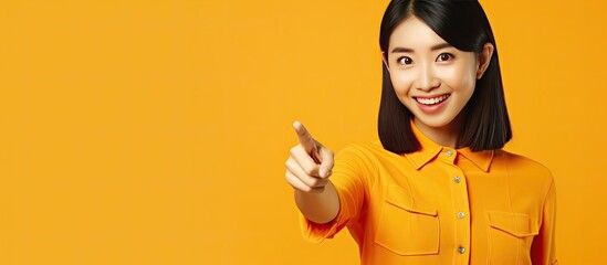 Poster - Young Asian woman in 30s wearing an orange shirt suggests product on yellow background