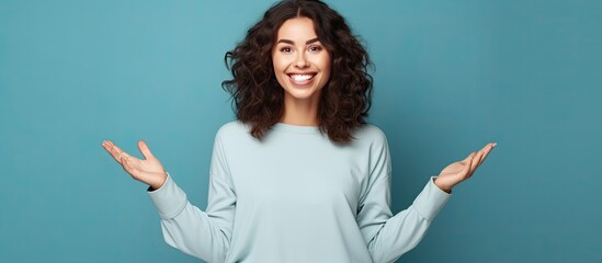 Wall Mural - Smiling young woman with brown hair pointing and presenting advertisement with open palms and excitement over blue background