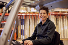 Portrait Of Smiling Female Operator Driving Forklift In Lumber Industry