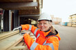© Maskot - Portrait of smiling female worker in protective workwear stacking planks at industry