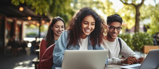 Multiethnic students happily doing homework outdoors with laptop smiling at camera