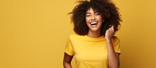 African American Woman With Curly Hair Laughs Points To Side With Torn Paper Wearing Black Shirt Isolated On Yellow Background