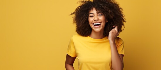 African American woman with curly hair laughs points to side with torn paper wearing black shirt isolated on yellow background