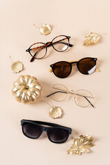 Wall Mural - Trendy sunglasses of different design and eyeglasses on beige background with golden leaves. Close up. Sunglass and spectacles sale concept. Optics shop fall promotion poster. Autumn Eyewear fashion