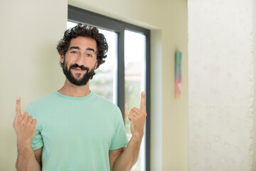 Wall Mural - young crazy bearded man feeling awed and open mouthed pointing upwards with a shocked and surprised look