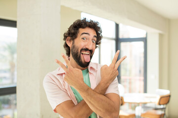 Wall Mural - young crazy bearded man smiling and looking happy, friendly and satisfied, gesturing victory or peace with both hands
