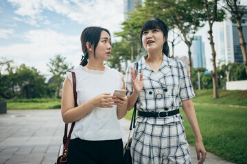 Two Asian businesswomen engage in a conversation on the street after their workday.