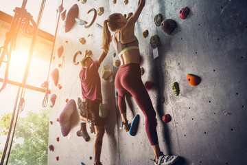 A strong couple of climbers climb an artificial wall with colorful grips and ropes.