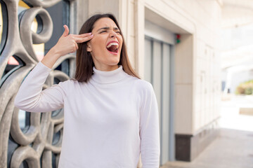 Wall Mural - pretty young adult woman looking unhappy and stressed, suicide gesture making gun sign with hand, pointing to head