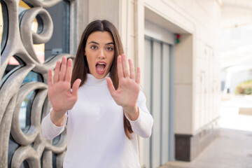 Wall Mural - pretty young adult woman feeling stupefied and scared, fearing something frightening, with hands open up front saying stay away