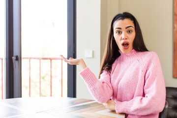 Wall Mural - pretty caucasian woman looking surprised and shocked, with jaw dropped holding an object with an open hand on the side