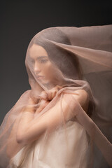 Poster - Brunette asian woman looking away while posing and touching beige fabric isolated on black