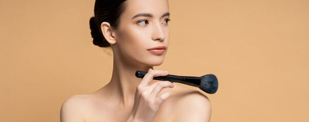 Poster - Asian woman with perfect skin holding cosmetic brush near naked shoulder isolated on beige, banner