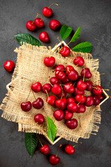 Wall Mural - Sweet red cherry on burlap on a black background. A large number of cherries with leaves on the table, on a black background. close-up.