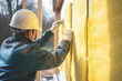 A construction worker is applying thermal insulation using glass wool panels in a wooden house.