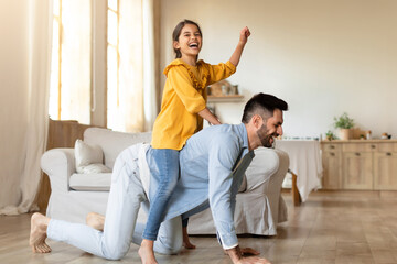 Happy Little Daughter Riding On Dad's Back At Home