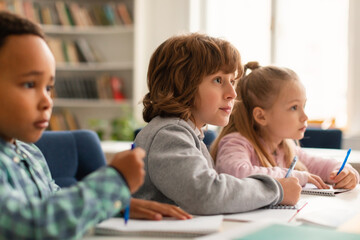 Poster - Elementary classroom of diverse children listening attentively to their teacher, writing in exercise notebooks