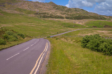 Wall Mural - 2023-06-13 A LONE LONELY COUNTRY ROAD WITH GREEN VEGETATION AND HILLS IN PORTEE SCOTLAND