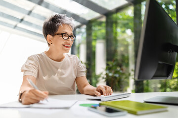 Creative mature woman employee working on research, using computer