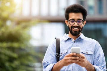 Wall Mural - Happy young eastern guy going home from office, using phone