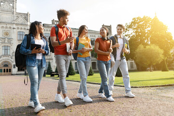 Five multiethnic students chatting and laughing while walking together at university campus