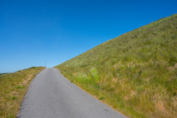 Sticker - Narrow asphalt road up a steep grass hill.