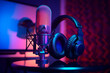 canvas print picture - A close-up of a microphone and headphones for podcasting or ASMR sounds on black stand in a neon led lighting, cyan and magenta, in a sound recording studio.