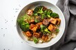 a quinoa bowl with steamed broccoli and smoked tofu cubes in teriyaki sauce with sesame seeds and green onions as topping on kitchen napkin, off-white light background, top view