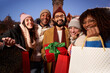 © CarlosBarquero - Portrait of group smiling multi-ethnic people showing Christmas winter shopping bags and gifts to camera. Photo happy young millennial friends posing cheerful outdoor. Relationships in community.