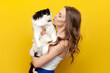 young cute girl kisses black and white cat on yellow isolated background and smiles, woman with pet