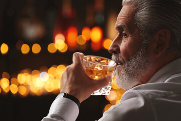 Sticker - Senior man drinking whiskey against blurred lights, closeup