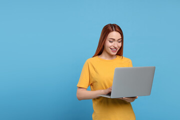 Smiling young woman working with laptop on light blue background, space for text