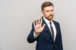 © DimaBerlin - Serious businessman showing stop hand gesture on grey background with copy space. No sign, not accepting deal in office at work, canceling contract. Not agreeing to statement or refusing agreement.
