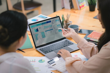 Two businesspeople or an accountant team are analyzing data charts, graphs, and a dashboard on a laptop screen in order to prepare a statistical report and discuss financial data in an office.