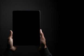 Hand holding tablet with mockup blank screen isolated on black background with copy space