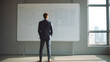 © AspctStyle - Back view of successful businessman in a suit standing in office with hands on his waist. Young successful businessman standing in front of whiteboard