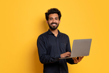 it business. indian man with laptop in hands posing on yellow background